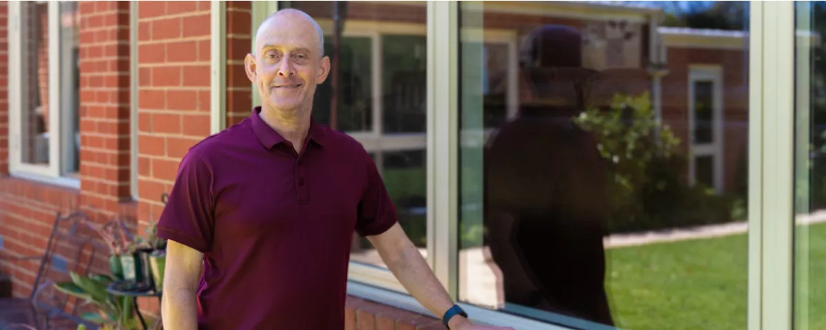 Man stands smiling next to windows outside home