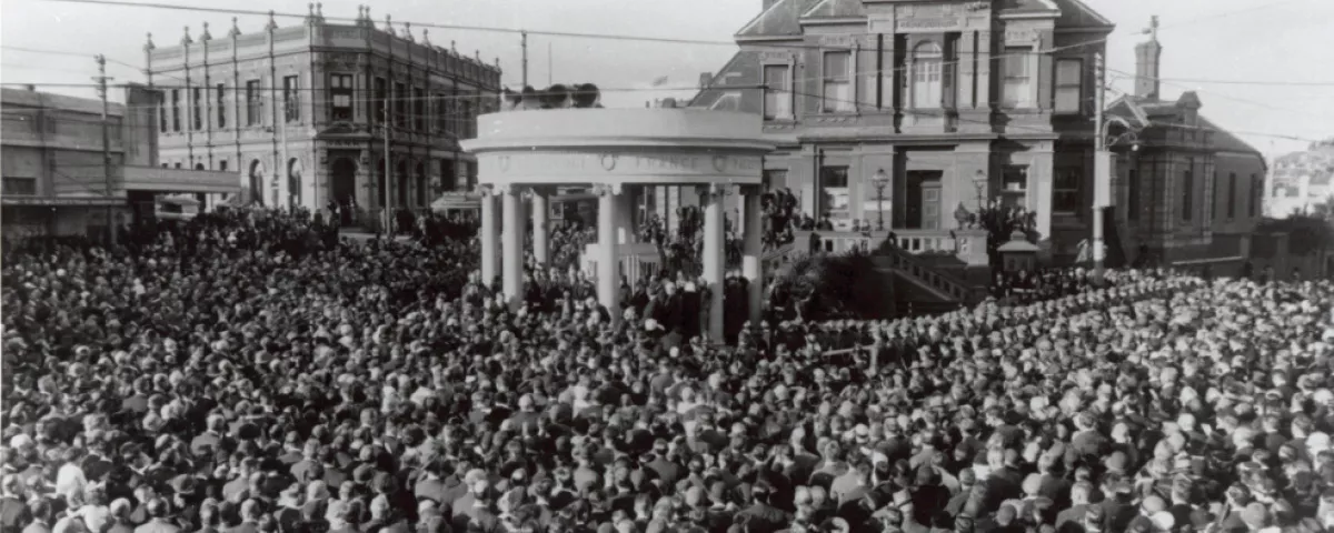 Black and white historical photo shows circular memorial surrounded by crowds of people