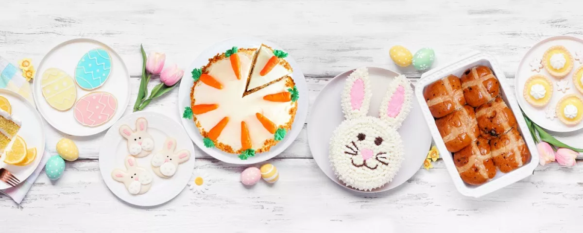 A table covered in Easter treats like bunny cake, hot cross buns and coloured eggs