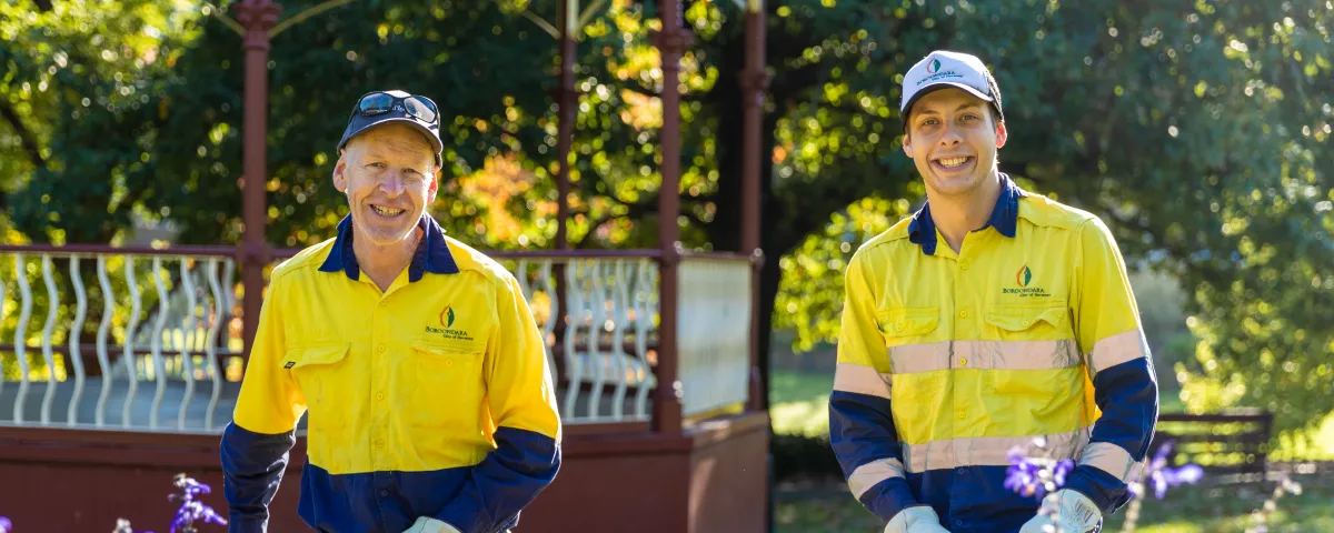 2 people in hi-vis holding whipper snippers in a garden