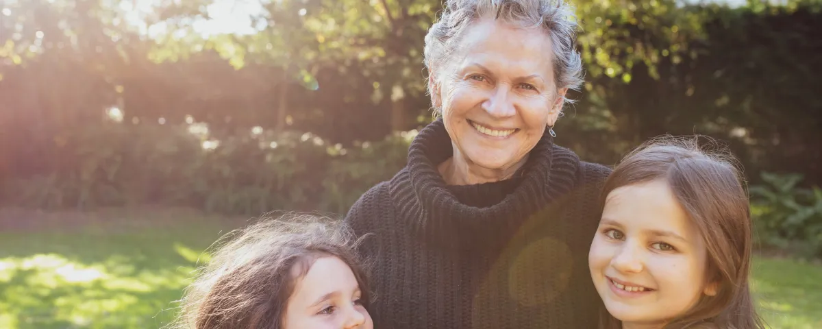 A friendly-looking older woman with her arms around 2 young girls in a garden