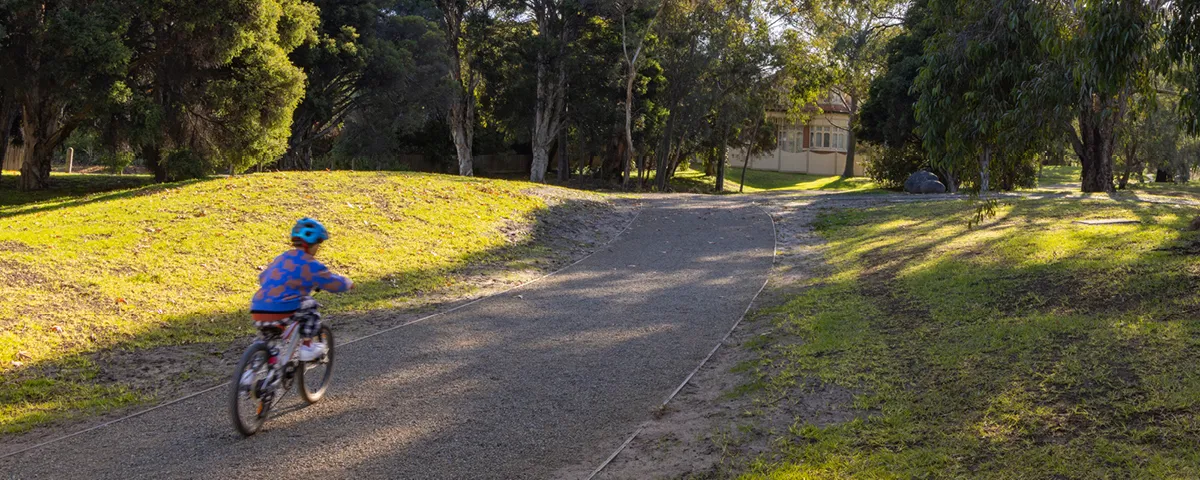 Small child rides bike on wide path with grass and trees on both sides