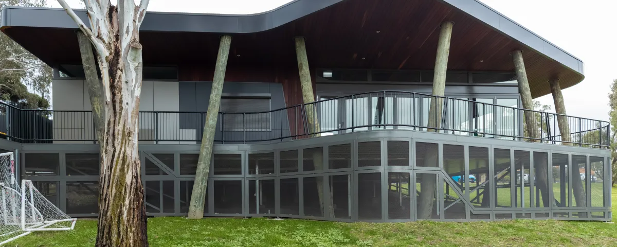 Outdoor pavilion in a park setting, with big glass windows and surrounded by green grass.