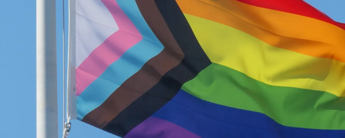 An LGBTQIA+ pride flag flying on a flag pole