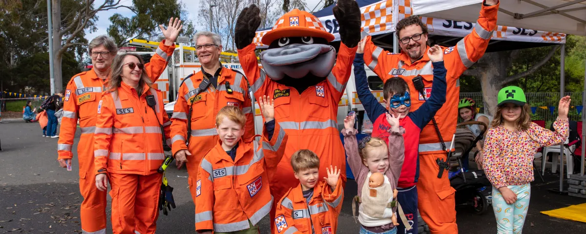 a group of people waving. They are wearing SES uniforms. In the middle of the group is the SES platypus mascot.