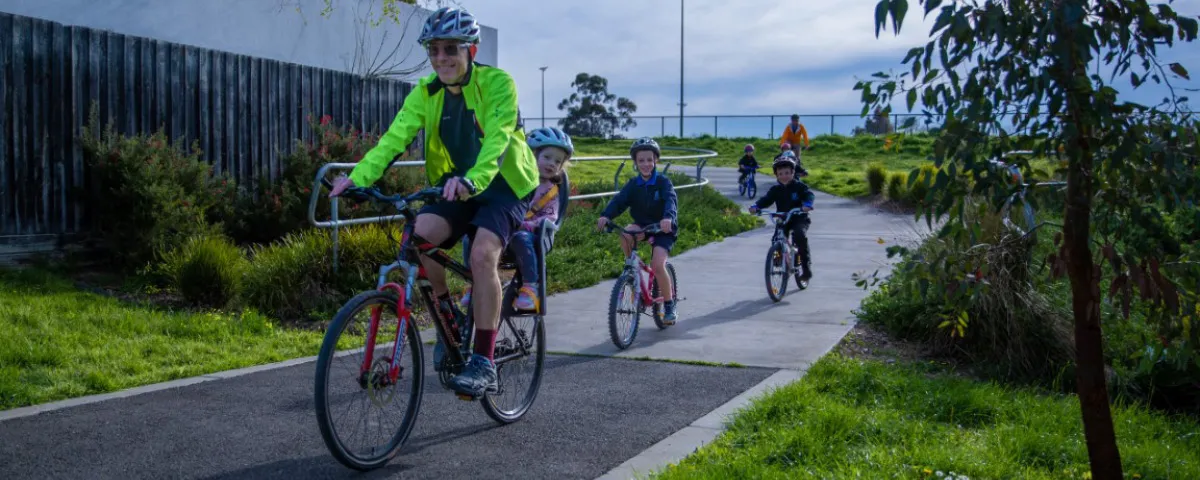 Smiling man rides bike on path followed by children on bikes
