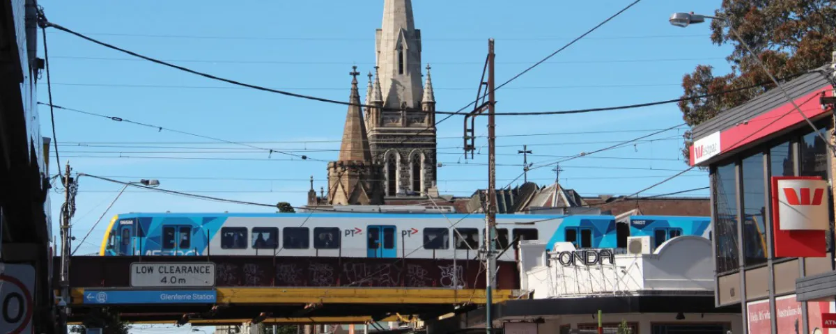 Train crosses rail bridge over Glenferrie Road with church spire in background