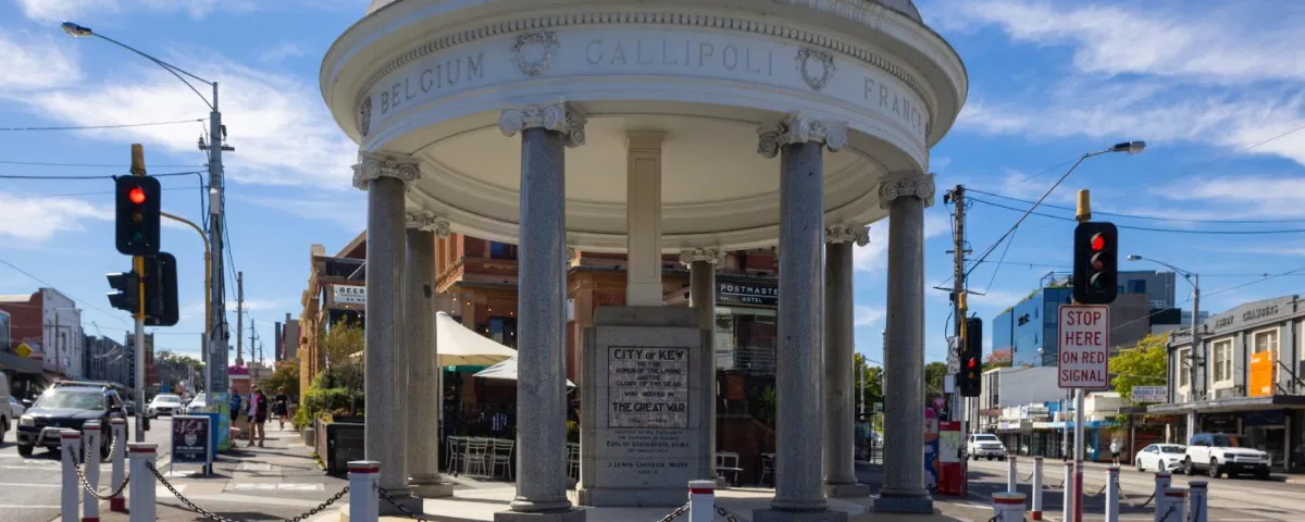 Street view of a cenotaph building on the edge of a roundabout with a historic building in background