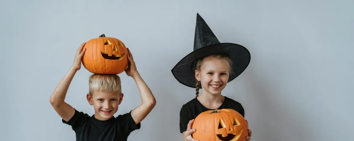 Two children wearing black are holding halloween pumpkins.