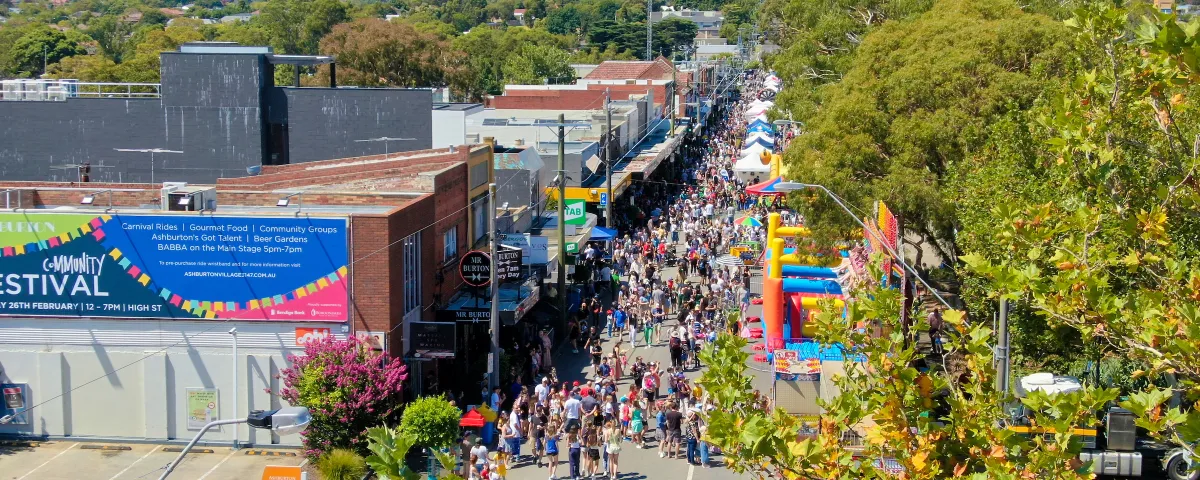 Ariel view of a tree lined shopping strip. the road is full of people attending a community festival