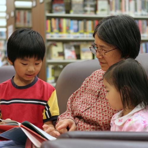 A young child reads to a grandmother and sibling