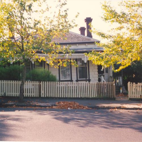 An old photograph of a heritage house, with view of the road and a car