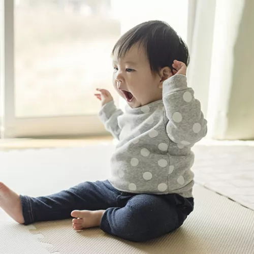 An older baby is sitting up and yawning