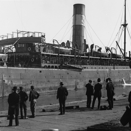 People on dock looking at steam ship in the water