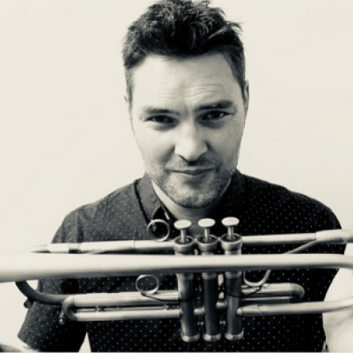 Musician Paul Williamson holding his trumpet out in front of him.