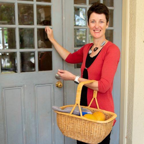 A woman knocking on a door with a basket of food around their arm