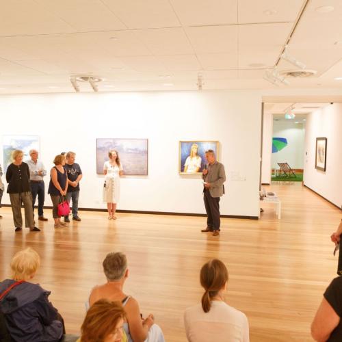 A group of people listening to a talk in a large gallery room with artworks on the walls