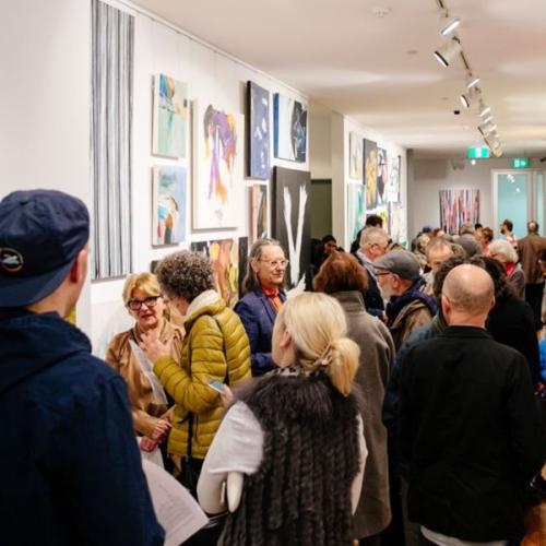 a crowd of people look at paintings hanging in a narrow gallery space