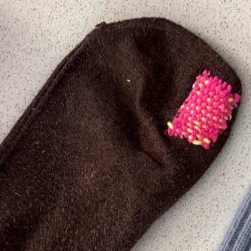 a brown woollen sock visibly darned with pink yarn