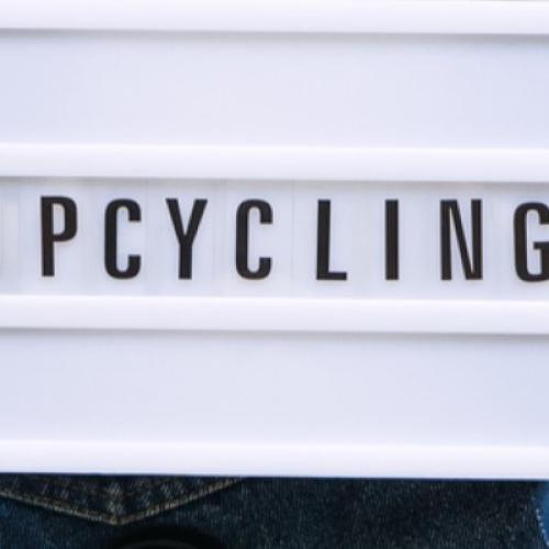 A lgiht up message board that says 'Upcycling', and is surrounded by pairs of jeans with scissors and measuring tape