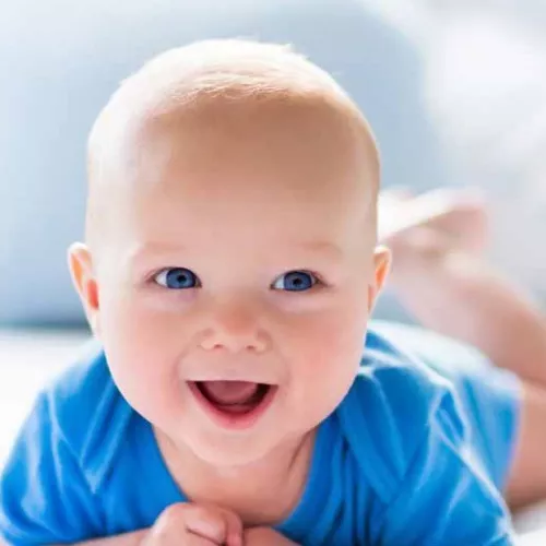 Smiling baby with blue eyes and blue clothing, lying on the stomach.