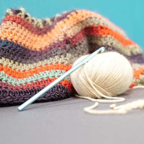 a ball of white yarn, a crochet hook and a piece of stripey crocheted material