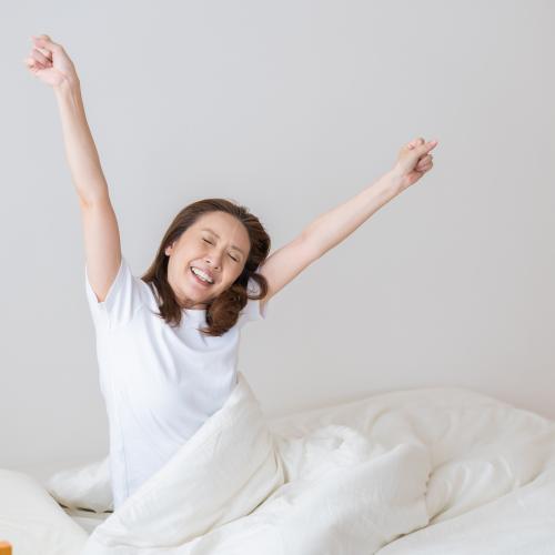a woman in bed stretches her arms up in the air and smiles 