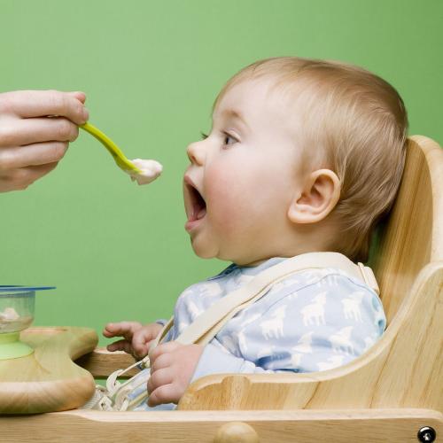 baby in high chair being fed food from a person off screen with solid food in bowl on highchair 