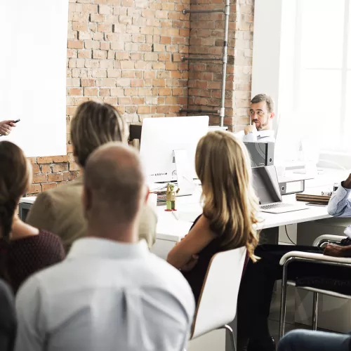 a woman lectures at a whiteboard before a room of adult students