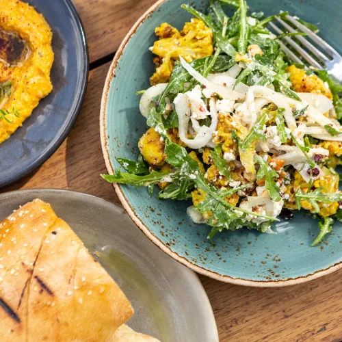 3 plates of food, a pasta dish with rocket and cauliflower, bread, and a bowl of dip.