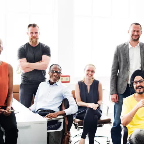a diverse group of people sitting and standing at desks