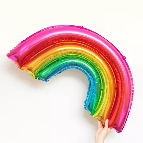 a foil balloon in the shape and colours of a rainbow being held up high by a hand