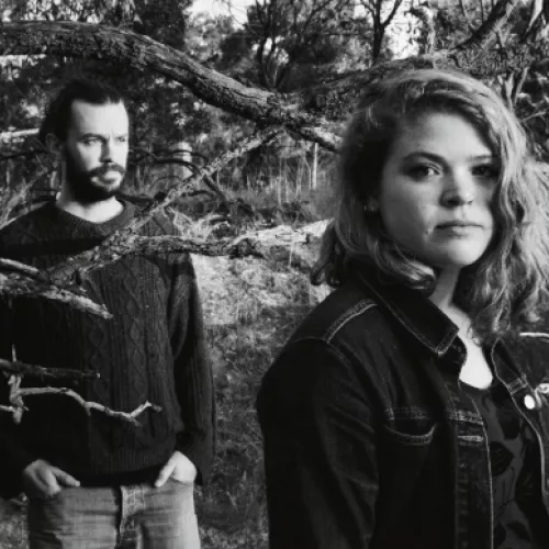Black and white image of Come Heavy Sleep performers Rosie Luby and Kier Stevens outside