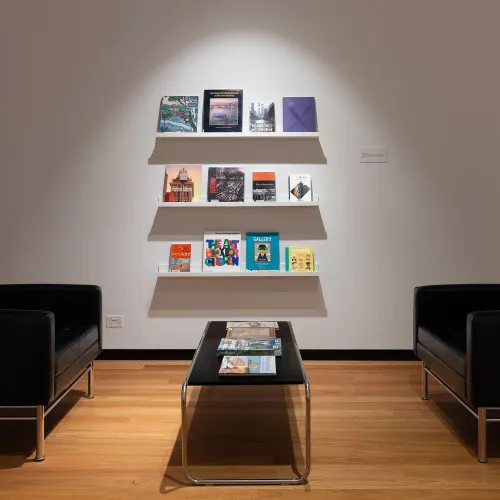 Shelves of art books displayed with tables and chairs within an art gallery. 