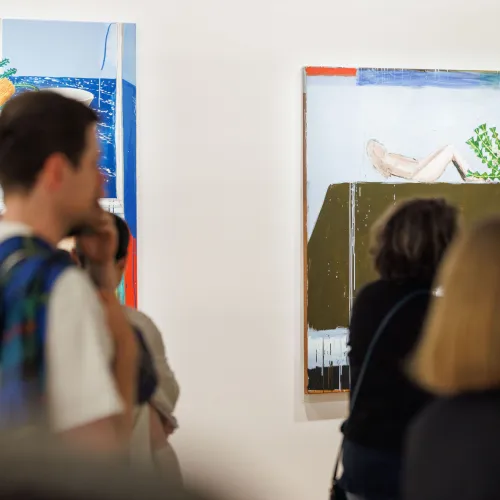 Visitors standing in front of two semi-abstract still life paintings at an exhibition tour. 