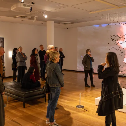 Visitors listening to artist Cyrus Tang speak about her artworks on display including a video of fire and a suspended sculpture of tiny pieces of a burnt piano. 