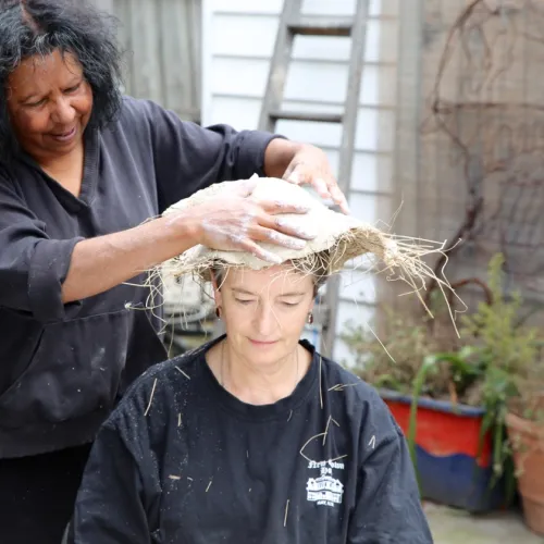 A woman places an Indigenous Australian mourning cap, kopi, on the head of another woman.