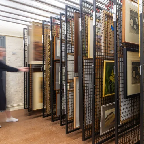 A photograph of blurry figure pulling out a rack of artworks