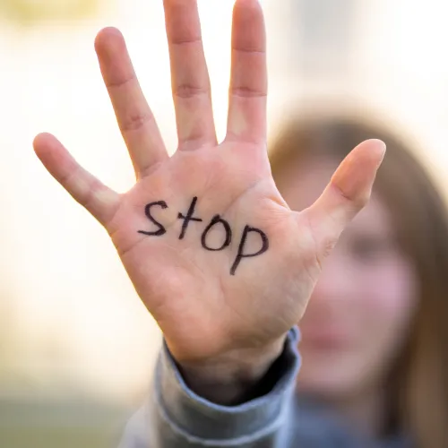 person with their hand reaching out showing their palm with the word 'stop' written on it.