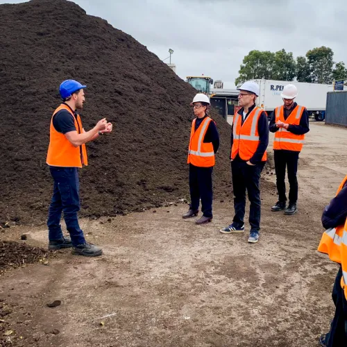People wearing hi-vis vests and hard hats stand at a landfill site