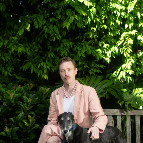 A person is sitting in front of a tree wearing a pink suit. They have a dog standing next to them