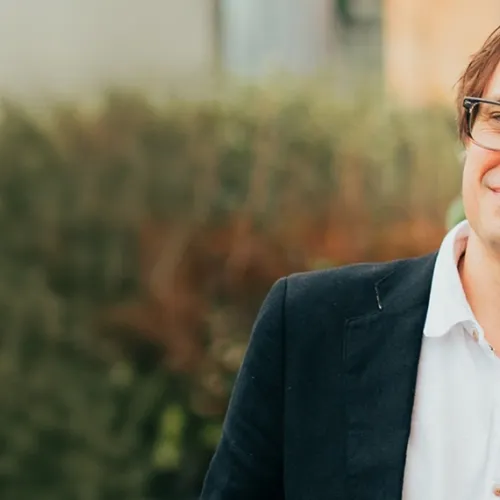 A person wearing glasses and short brown hair is smiling at the camera