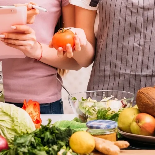 A bench covered in fruit and vegetables. a group of people are looking at a recipe book and taking notes.