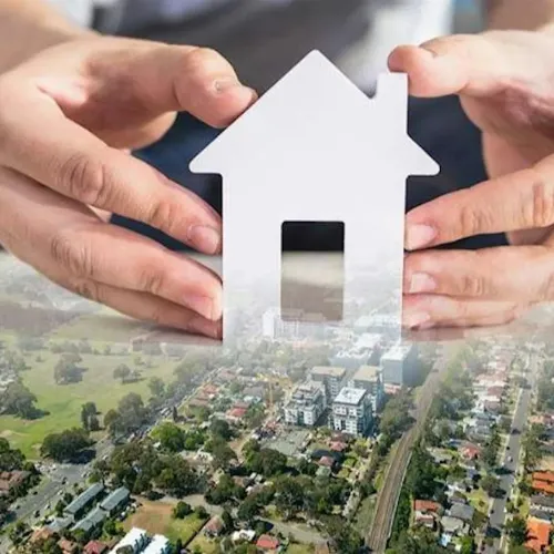 Two hands holding a white cut out house shape over a suburban landscape.