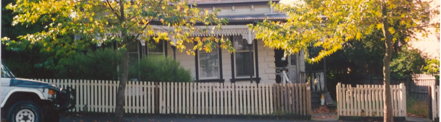 An old photograph of a heritage house, with view of the road and a car