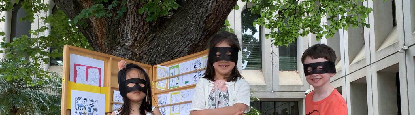 Three children wear black eye masks standing infront of their book display