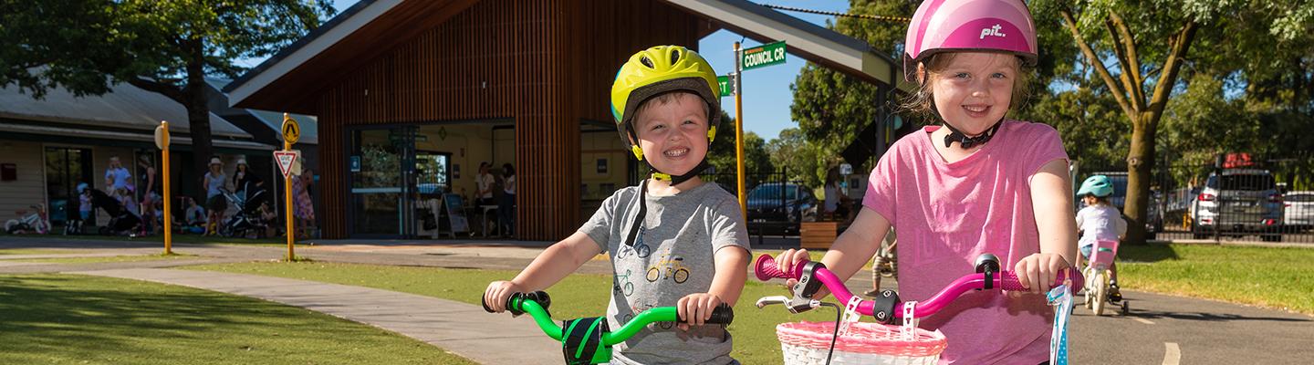 A boy and girl on their bikes smile at the camera at Kew Traffic School