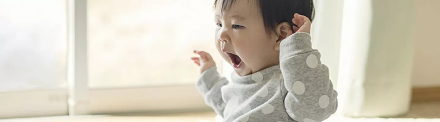 An older baby is sitting up and yawning