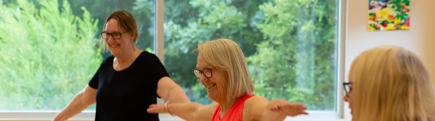 3 older adults exercising with the aid of chairs.