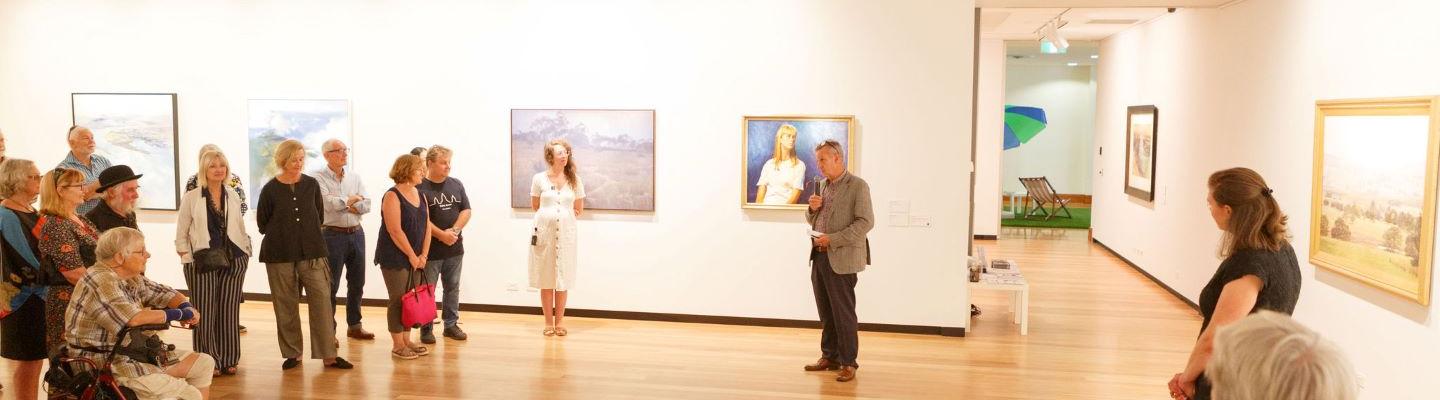 A group of people listening to a talk in a large gallery room with artworks on the walls